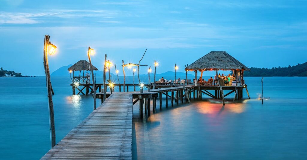 Illuminated pier and bungalow on a tranquil tropical sea at twilight.