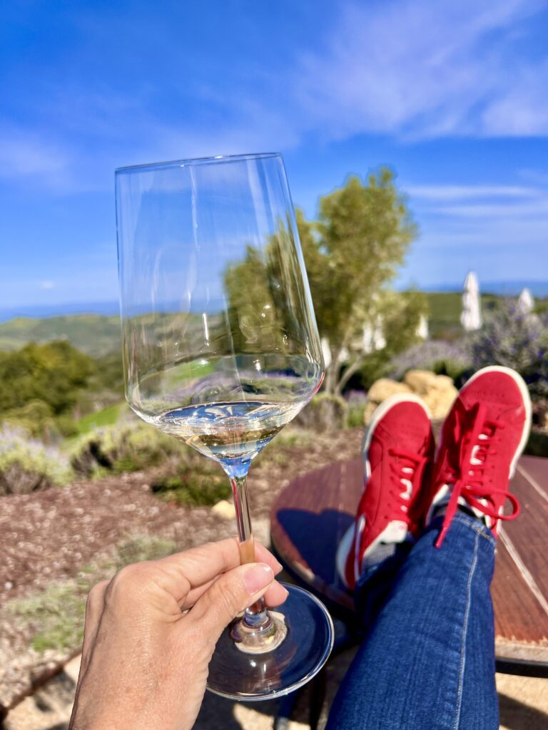 Person relaxing outdoors holding an empty wine glass with red shoes visible.