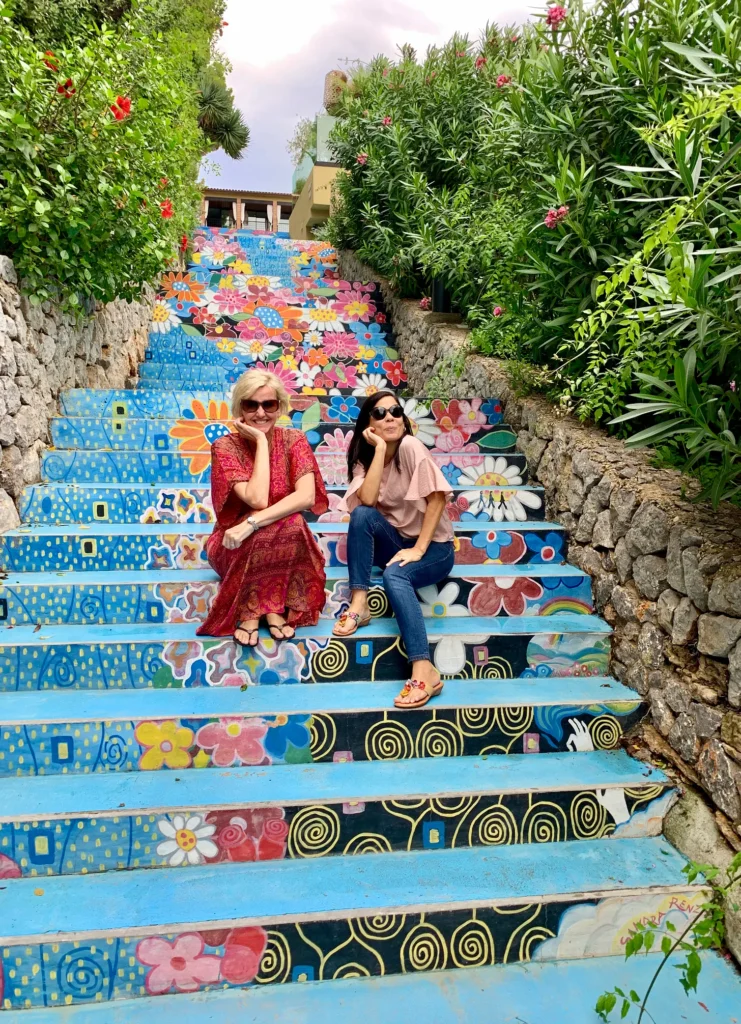 Two women sitting on beautifully decorated mosaic stairs outdoors.