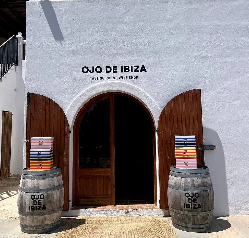 Entrance of Ojo de Ibiza with wooden doors and wine barrels.