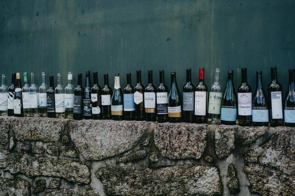 A variety of wine bottles displayed on a rustic stone wall, captured outdoors for a vintage feel.